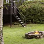 Fire pit in the garden in front of a house with wooden terrace and stairs.
