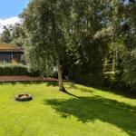 Green garden with fire pit and trees. House with roof in background.
