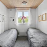 Two beds with gray quilt, wooden ceiling, and window with flowers.