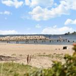 Beach with rock breakwater and wooden pier. People swim and enjoy the view.