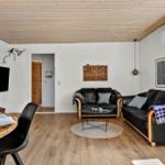 Living and dining area with wooden floor, black sofas, and TV mounted on the wall.