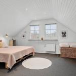 Schlafzimmer mit Dachschrägen, Bett, zwei Fenstern und Korb.