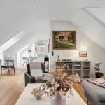 Wohnzimmer mit Dachschrägen, Holzboden und Möbeln. Wandbild und Pflanzen sichtbar.