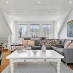 Wohnzimmer mit grauem Sofa, weißem Tisch und Fenstern.