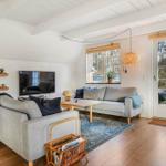 Wohnzimmer mit grauem Sofa, Holzboden und Fenster zur Außenterrasse.