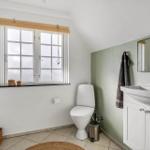 Badezimmer mit Toilette, Waschbecken und Fenster mit Jalousie.