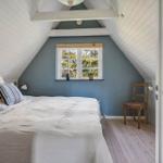 Schlafzimmer mit Dachschrägen, Bett, Stuhl und Fenster mit Blick auf Bäume.