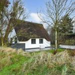 Weiße Hütte mit strohgedecktem Dach, umgeben von Bäumen und Gras.