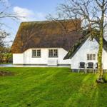 Wohnhaus mit Strohdach und grünem Rasen. Außentisch mit Stühlen unter Bäumen.