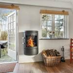 Raum mit Kamin, Fenster und Tür zum Garten. Holzstuhl und Korb mit Brennholz.