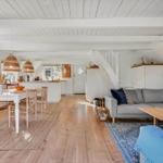 Wohn- und Essbereich mit Holzboden, Sofa und Tisch. Weiße Wände und Decke mit Holzbalken.