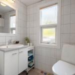 Bathroom with sink, mirror, toilet, and window.