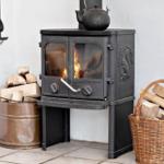 Black wood-burning stove with fire, metal bucket, and wicker basket with firewood.