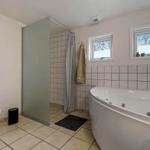 Badezimmer mit Badewanne, Dusche und Toilette. Fenster mit Blick nach draußen.
