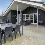 Außenbereich mit Tisch, Stühlen und Grill. Schwarze Holzwand und Terrasse.