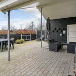 Terrasse mit Tisch, Stühlen und Sitzgruppe unter Markise. Grill und Pflanzen sind vorhanden.