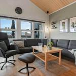 Wohnzimmer mit Sofa, Sessel und Tisch. Große Fenster und Holzdecke.