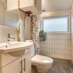 Badezimmer mit Waschbecken, Toilette und Dusche. Fenster und Pflanze sichtbar.