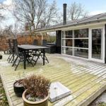 Terrasse mit Tisch, Stühlen und Grill. Glasfront führt ins Haus.