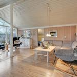 Wohnzimmer mit Sofa, Schaukelstuhl und Holzboden. Große Fenster und Holzwände.