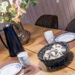 Holztisch mit Stühlen, Teller, Kaffeekanne und Brotkorb.