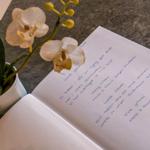 Ein Buch mit handschriftlichem Text und eine Orchidee auf einer Arbeitsfläche.