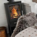 Holzofen mit brennendem Feuer, Tisch mit Polster und Glas