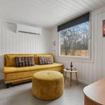 Gelber Sofa und Sitzhocker im Wohnbereich mit Fenster und Wandheizung.