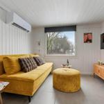Ein Wohnzimmer mit gelbem Sofa, runden Sitzkissen und Holzmöbeln.