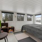 Schlafzimmer mit Bett, Stuhl und Fenstern. Wand mit Holzverkleidung und Einrichtungsgegenständen.