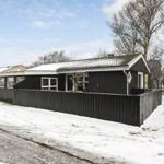 Schwarzes Haus mit Schnee bedecktem Dach und Holzzaun.