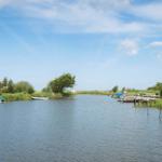 Ein ruhiger Kanal mit Booten und Ufervegetation unter blauem Himmel.