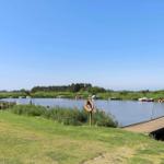 Holzsteg führt zu einem See mit Booten und Grünflächen.