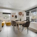 Esszimmer mit runden Tisch, Stühlen und Fensterblick. Kaminofen und gelber Sitzbereich.