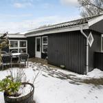 Schwarzes Haus mit weißem Dachrand und Terrasse im Schnee.