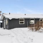 Black wooden house with snow-covered roof and white window frames.