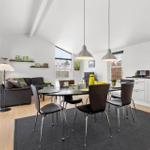 Living and dining area with table, chairs, and sofa. Windows and light walls.