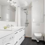 Bathroom with shower, sink, and toilet. White tiles and black floor tiles.