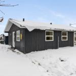Black wooden house with snow-covered roof and white window frames.