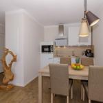 Essbereich mit Tisch, Stühlen und Küchenzeile. Dekorative Holzskulptur links.