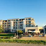 Modernes Mehrfamilienhaus mit Balkonen und Außenbereich mit Tischen und Stühlen.