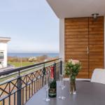 Balcony with table, glasses, and flowers overlooking the sea and buildings.