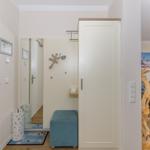 Eingangsbereich mit Garderobe, Sitzhocker und Blick in Wohnzimmer mit Sofa.