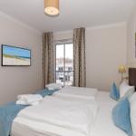 Schlafzimmer mit Doppelbett, TV und Balkonansicht.