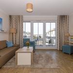 Wohnzimmer mit Sofa, Couchtisch und Balkon. Fernseher und Gardinen sichtbar.