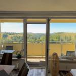 Terrasse mit Blick auf grüne Hügel. Im Innenraum Tisch, Stühle und Bodenfliesen.