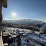 Schneebedeckter Blick auf einen Park mit Spielplatz und Bäumen unter blauem Himmel.