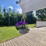 Terrasse mit Blumenkorb, Spielgerüst und grünem Rasen im Hintergrund.