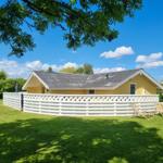 Ein gelbes Haus mit weißer Umzäunung und Gartenliegen unter blauem Himmel.