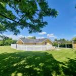 Ein gelbes Haus mit Garten, weißer Umzäunung und Liegestühlen unter Bäumen.